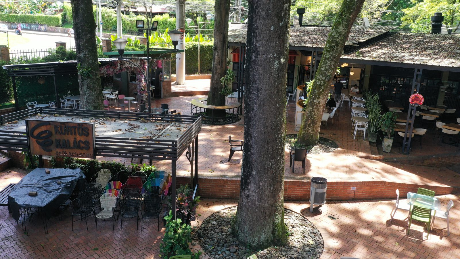 Vista de la plazoleta con árboles, mobiliario exterior y fachadas comerciales